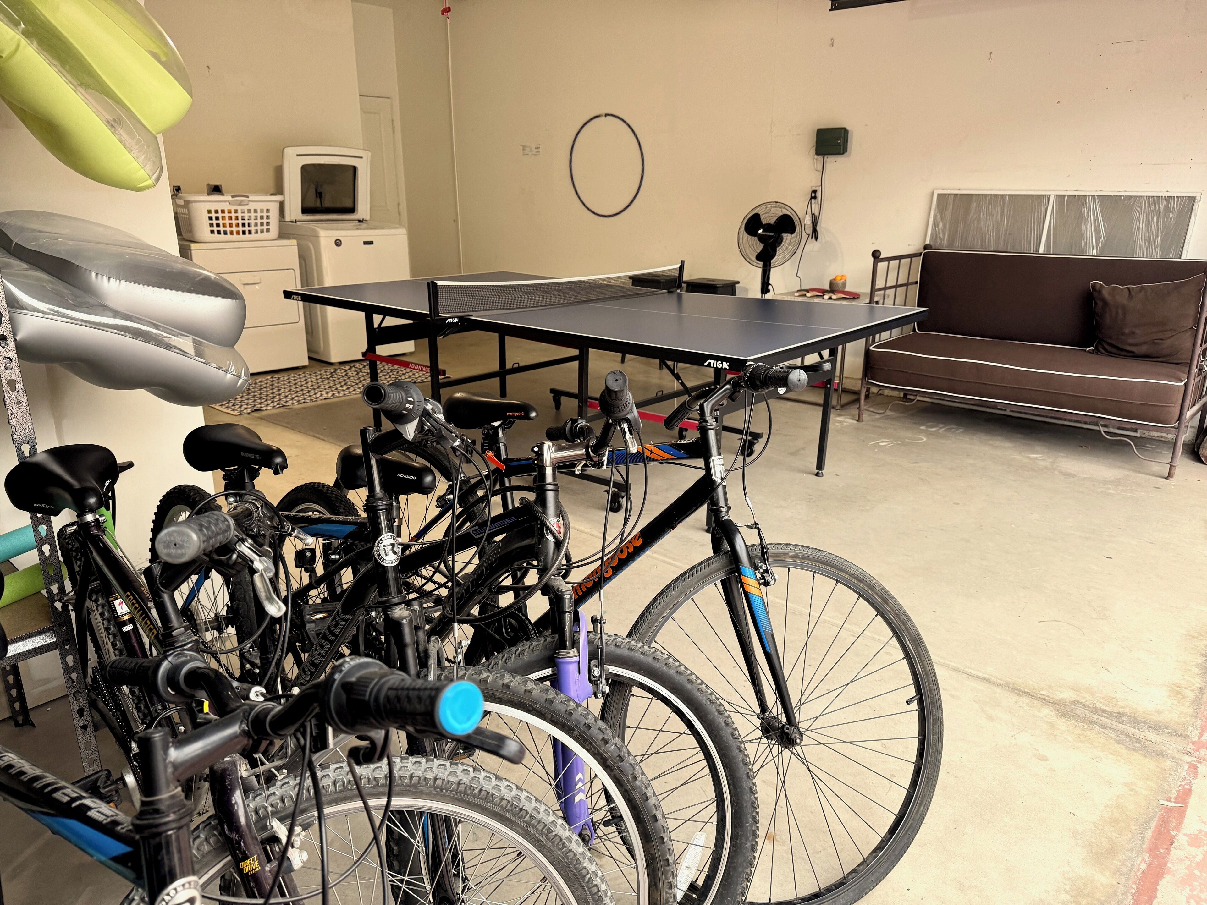 Una habitación con bicicletas, mesa de ping pong, sofá y lavadora.