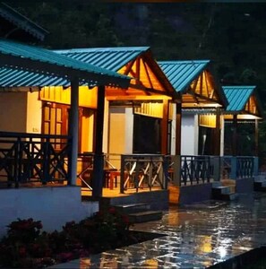 A series of traditional-style buildings with wooden structures and blue roofs, connected by a waterway. - Anant Vilas Resort (Nainital)