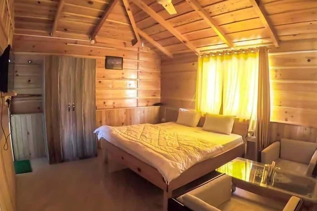 A wooden cabin bedroom with a bed, a small table, and a chair.