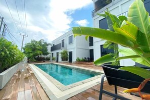 A swimming pool with a wooden deck, surrounded by potted plants and a modern building. - Onyx Hotel & Villa (Bintan)
