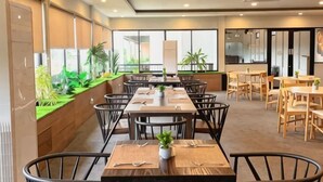 A dining area with multiple tables and chairs, large windows, and indoor plants. - Onyx Hotel & Villa (Bintan)