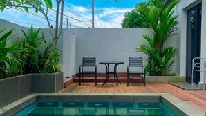 A pool with two chairs and a table, surrounded by plants and a white wall. - Onyx Hotel & Villa (Bintan)