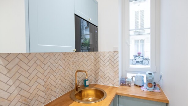Et moderne køkken med et backsplash af fiskebensmønstrede fliser, en rustfri stålvask og et vindue med udsigt til en gade.