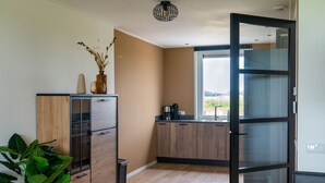 A modern kitchen with wooden cabinets, a coffee machine, and a large window offering a view of the outdoors. - Villa in Leons near Frisian Lakes (Leons)