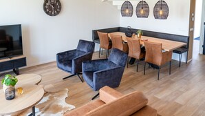 A modern living room with a sofa, a coffee table, and a TV. There is a dining area with a table and chairs. - Villa in Leons near Frisian Lakes (Leons)