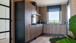 A modern kitchen with wooden cabinets, a built-in oven, and a window with a view of the outdoors. - Villa in Leons near Frisian Lakes (Leons)