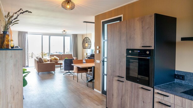 A modern kitchen with wooden cabinets, a built-in oven, and a dining area with a table and chairs. - Villa in Leons near Frisian Lakes (Leons)