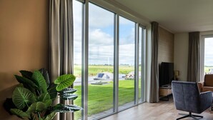 Ein geräumiges Zimmer mit großen Fenstern, einem modernen Sessel, einem Fernseher und einer Topfpflanze.