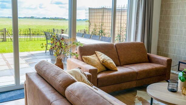 Ein modernes Wohnzimmer mit einer Ledersofa, einem runden Couchtisch und Blick auf ein grünes Feld durch große Fenster.