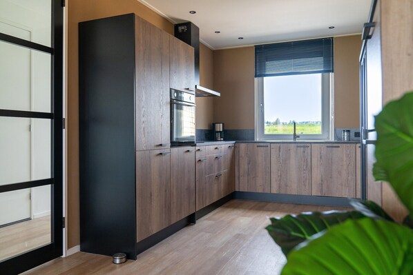 Een moderne keuken met houten kastjes, een inbouwoven en een raam met uitzicht op de omgeving.