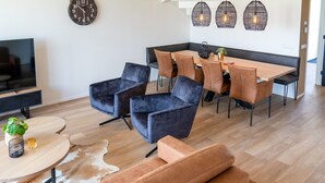 Ein modernes Wohnzimmer mit Fernseher, Sitzgelegenheiten, einem Essbereich und einer Uhr an der Wand.