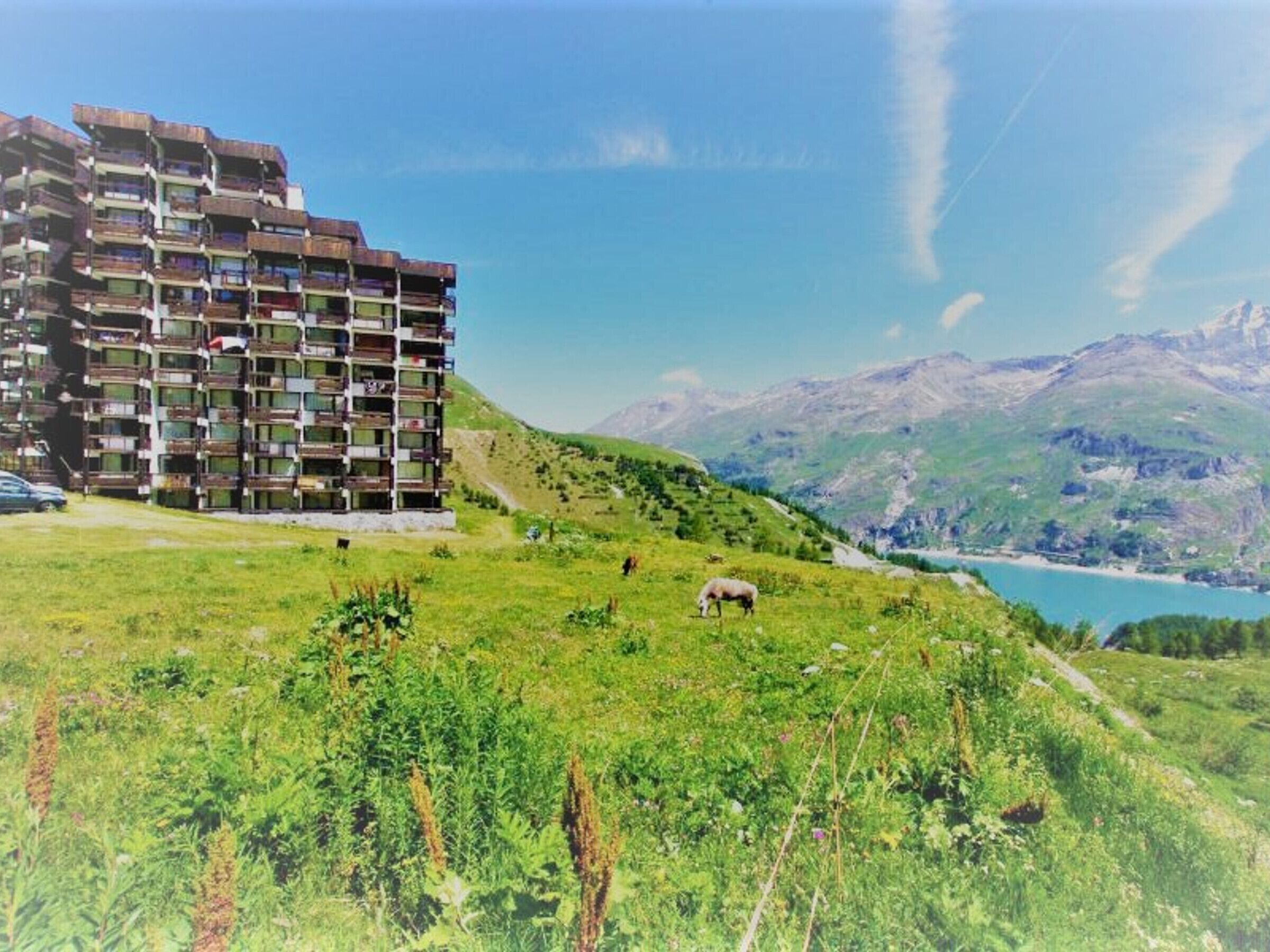 A multi-story building with balconies, set against a mountainous backdrop and a clear sky.