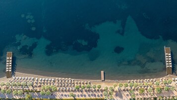Μια αεροφωτογραφία μιας παραλίας με μια σειρά από ξαπλώστρες και φοίνικες.