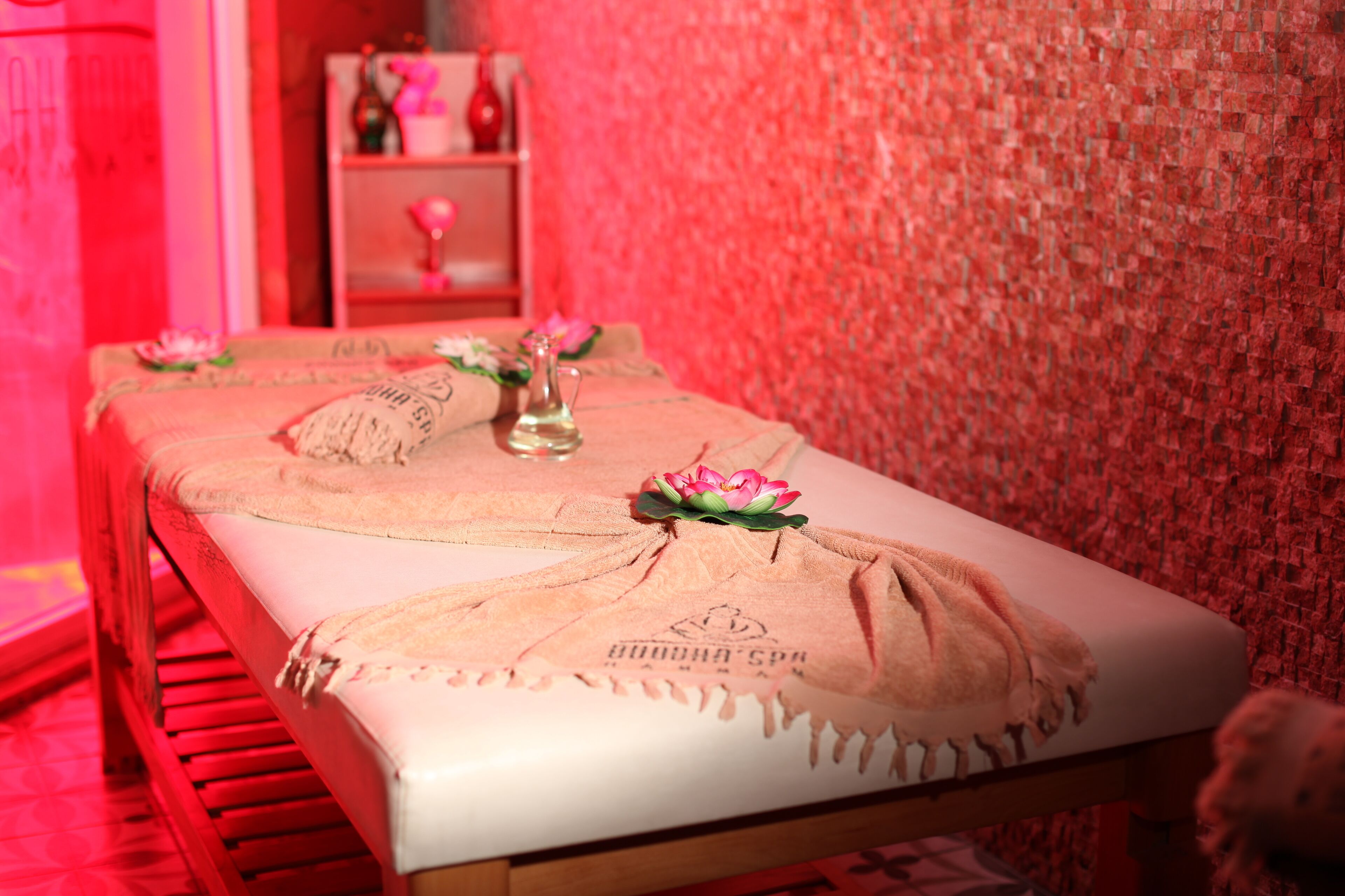 A neatly arranged room with a bed, a small table with a vase and flowers, and a shelf with decorative items.