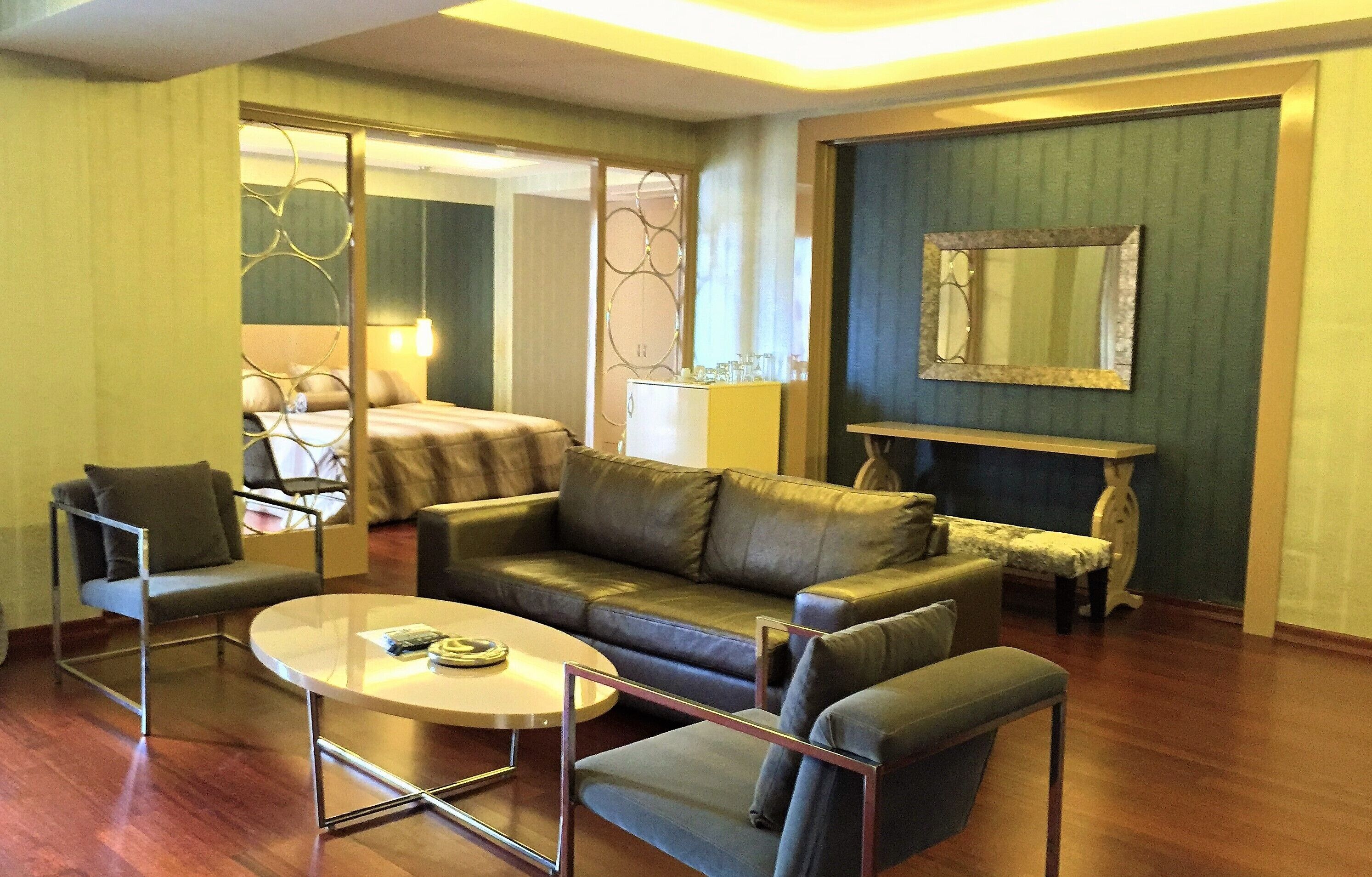 A modern hotel room with a leather sofa, a glass coffee table, and a bed with a headboard.
