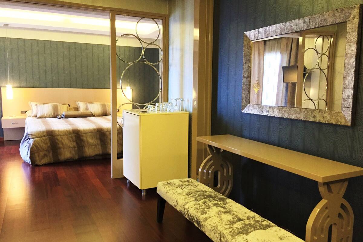 Una habitación de hotel con cama, un escritorio pequeño, un banco y un espejo.