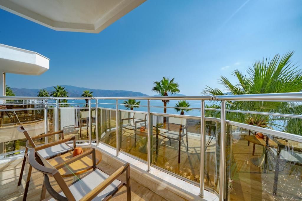 A balcony with glass railings, outdoor furniture, and a view of the sea and mountains.