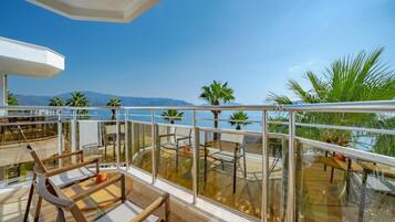 A balcony with glass railings, outdoor furniture, and a view of the sea and mountains.