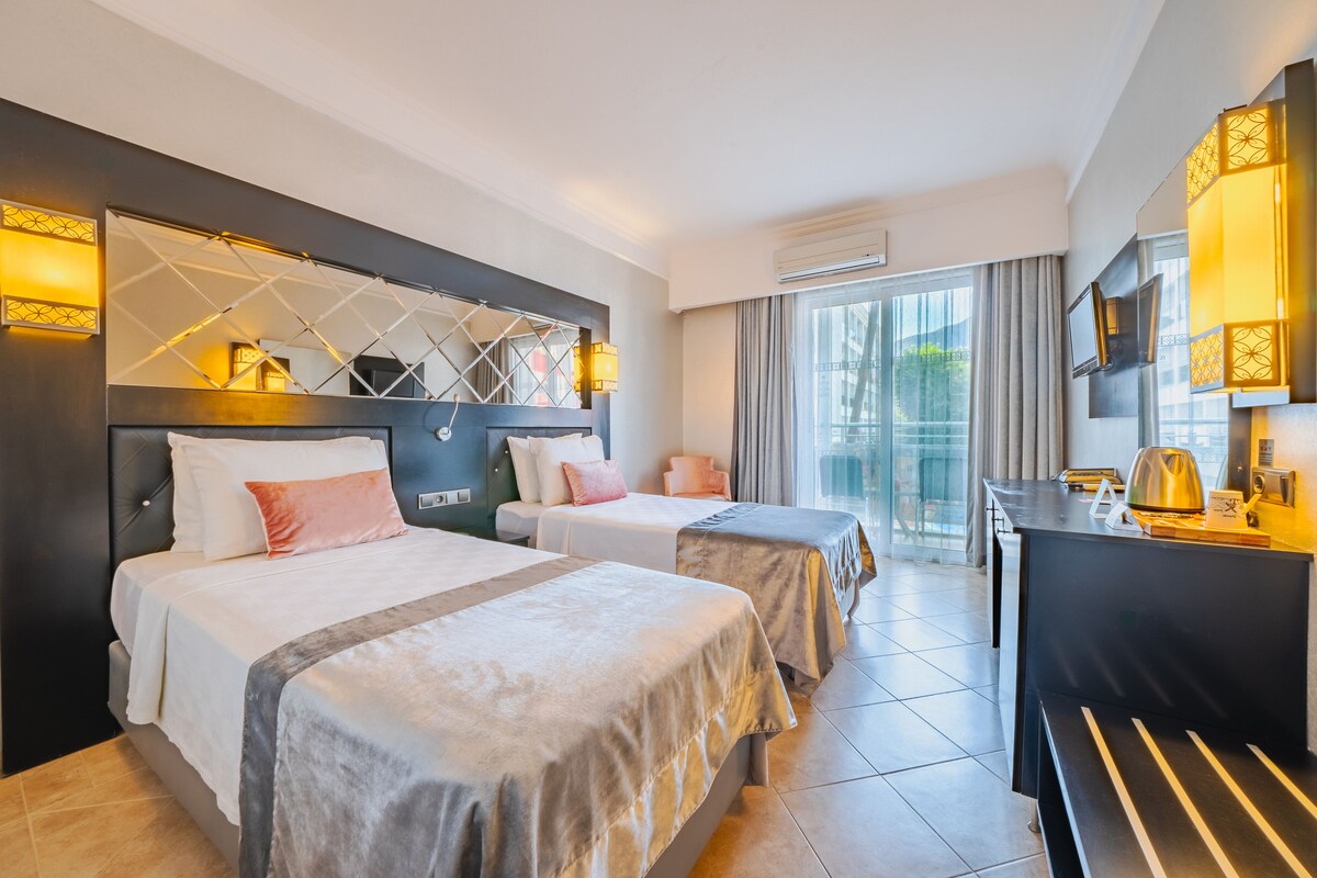 Ein Hotelzimmer mit zwei Betten, einem Schreibtisch und einem großen Fenster mit Vorhängen.