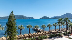 A beach resort with palm trees, thatched umbrellas, and a view of the sea and mountains. - Prime Beach Hotel - All inclusive (Marmaris)