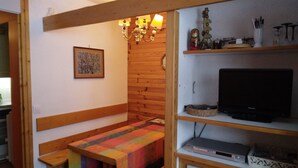 A cozy room with a wooden bench, a television on a shelf, and a wall-mounted clock.