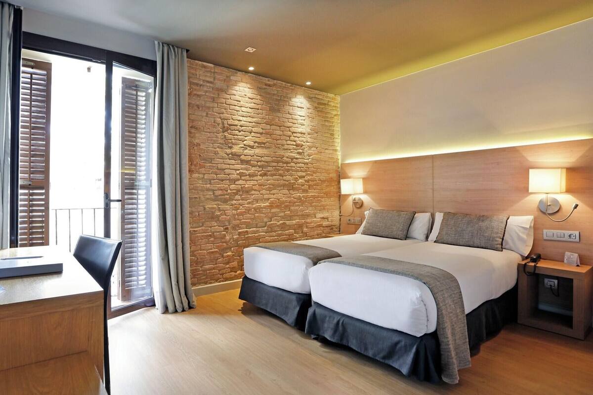 A hotel room with a large bed, a desk, and a view through a sliding door.