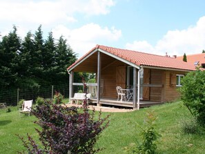 Een houten chalet met een overdekte veranda, een omheinde tuin en een kleine tafel met stoelen.