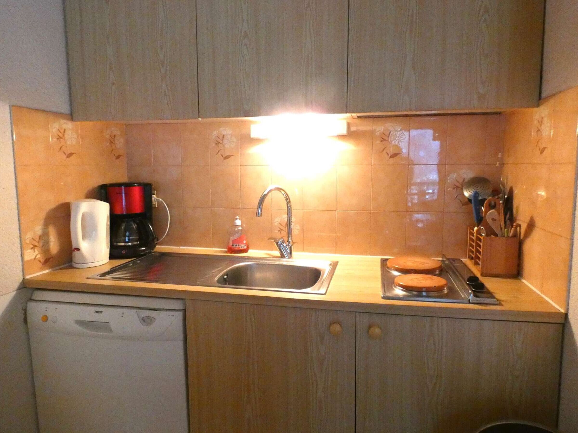A kitchen with a sink, a coffee maker, a dish soap bottle, and a utensil holder.