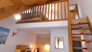 Un escalier en bois menant à un niveau supérieur, un coin cuisine avec des placards et un four à micro-ondes, et une petite fenêtre avec vue.