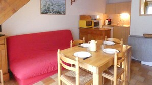 Une pièce chaleureuse avec un canapé rouge, une table à manger en bois et un coin cuisine équipé d’un four à micro-ondes et d’une machine à café.
