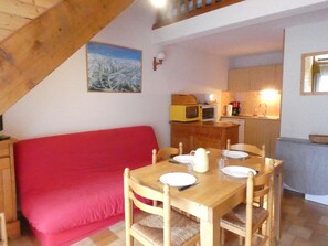 A cozy room with a red sofa, wooden dining table, and a kitchen area with a microwave and coffee maker.
