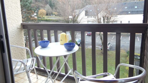Un balcon avec une table et des chaises, donnant sur un quartier résidentiel et des collines.