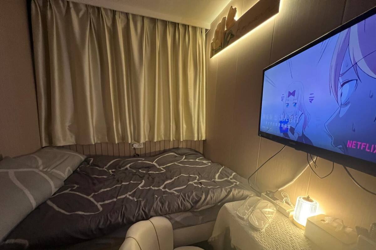 Une chambre d’hôtel avec un lit, un bureau équipé d’un ordinateur et un téléviseur fixé au mur qui diffuse une émission.