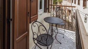 A balcony with two tables and chairs, a window, and a view of neighboring buildings.