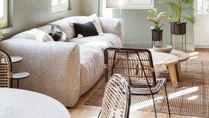 A cozy room with a bed, a dining table, chairs, a hanging light fixture, and potted plants.