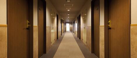 A long, narrow hotel corridor with wooden doors on both sides and a carpeted floor.