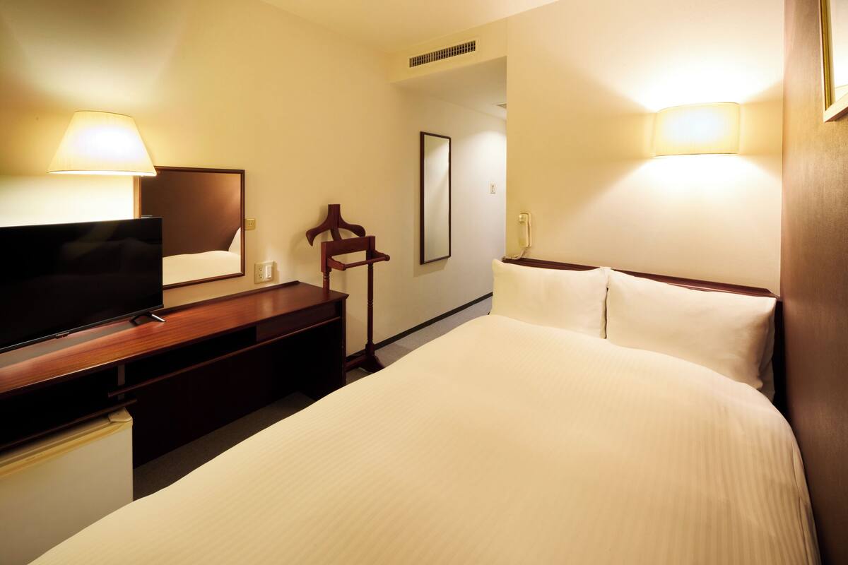 A hotel room with a bed, a TV, a desk, and a lamp.