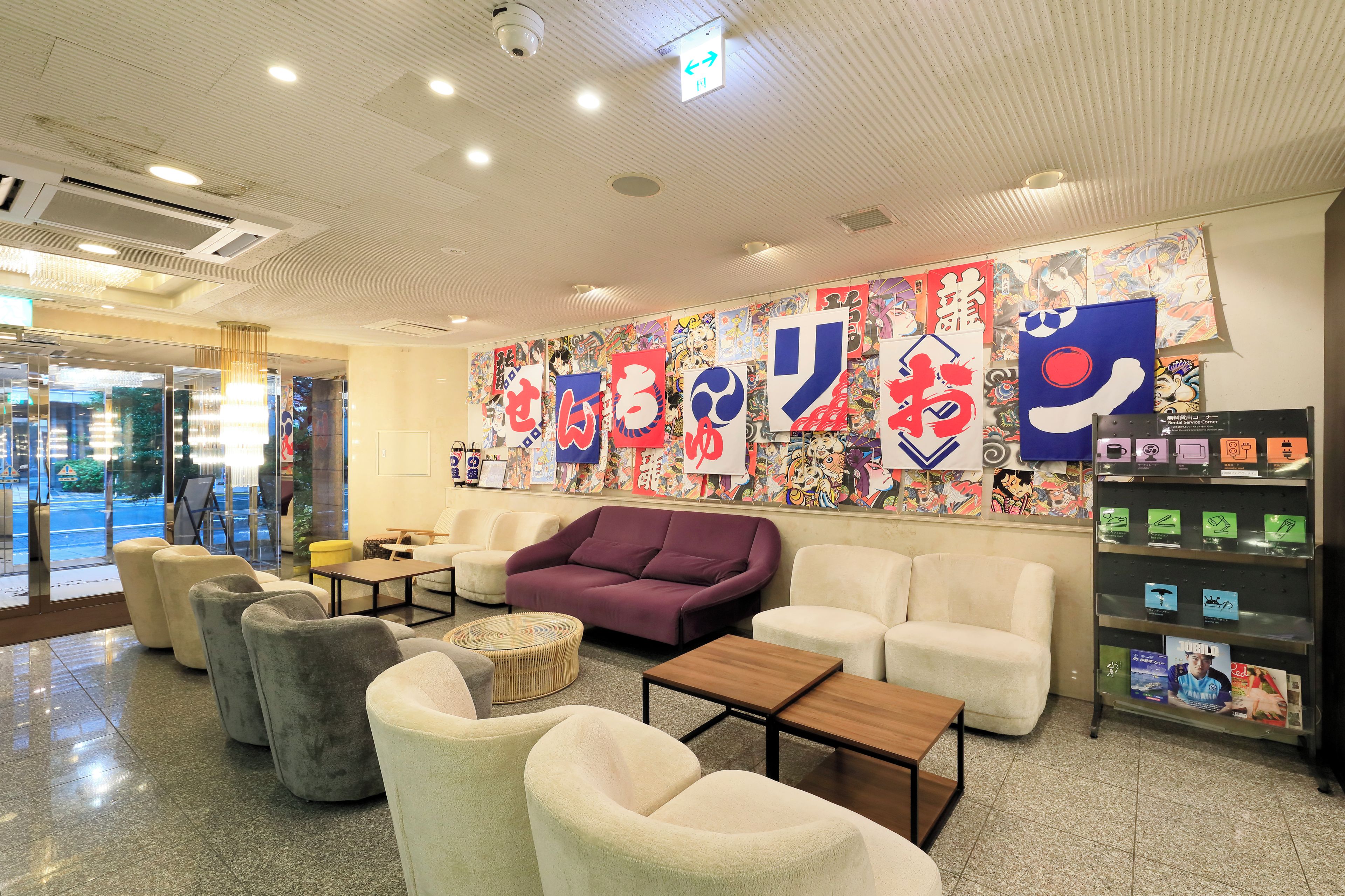 A hotel lobby with seating areas, a reception desk, and a wall decorated with colorful artwork.