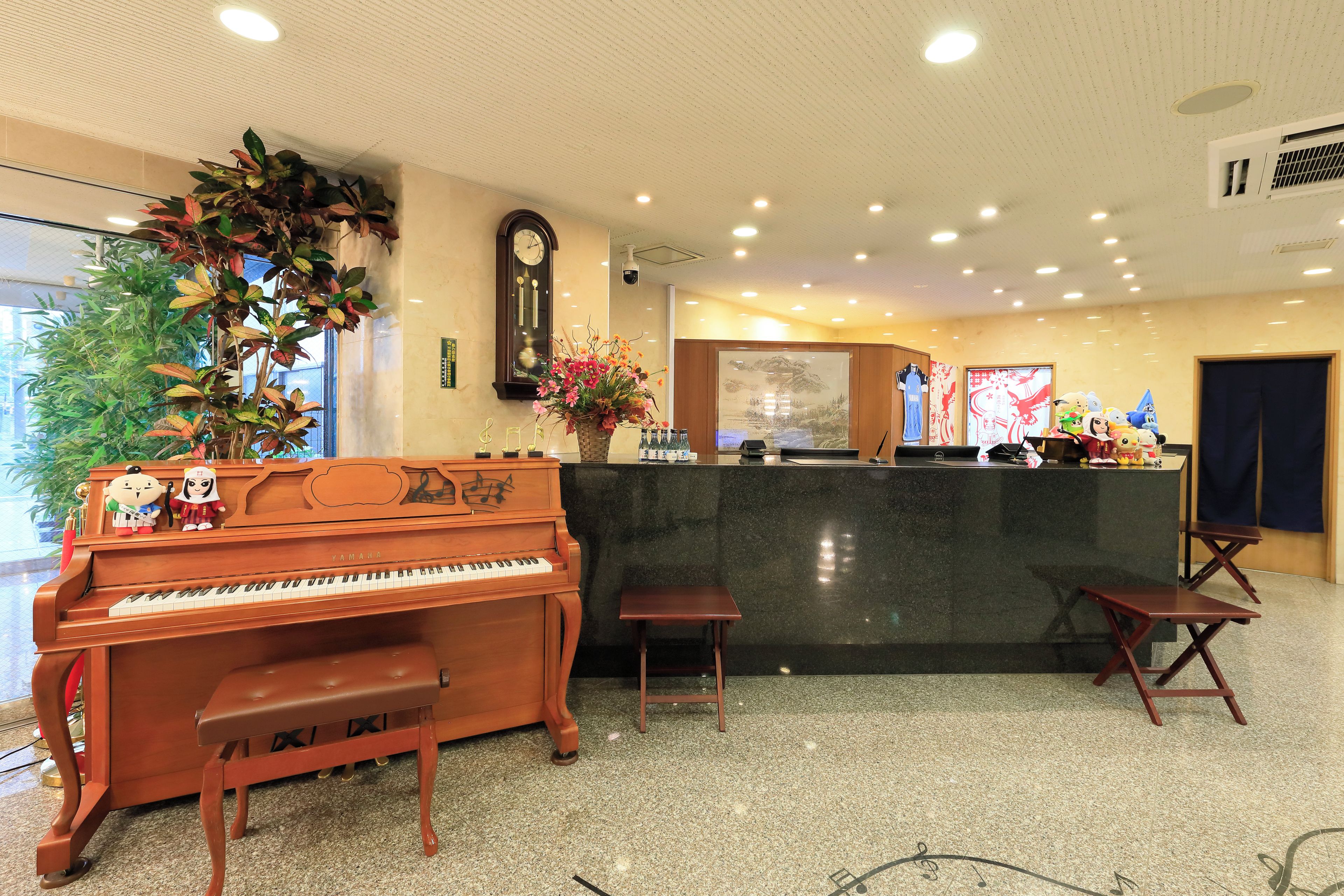 Un área de recepción con un piano, un banco, una planta y un reloj en la pared.