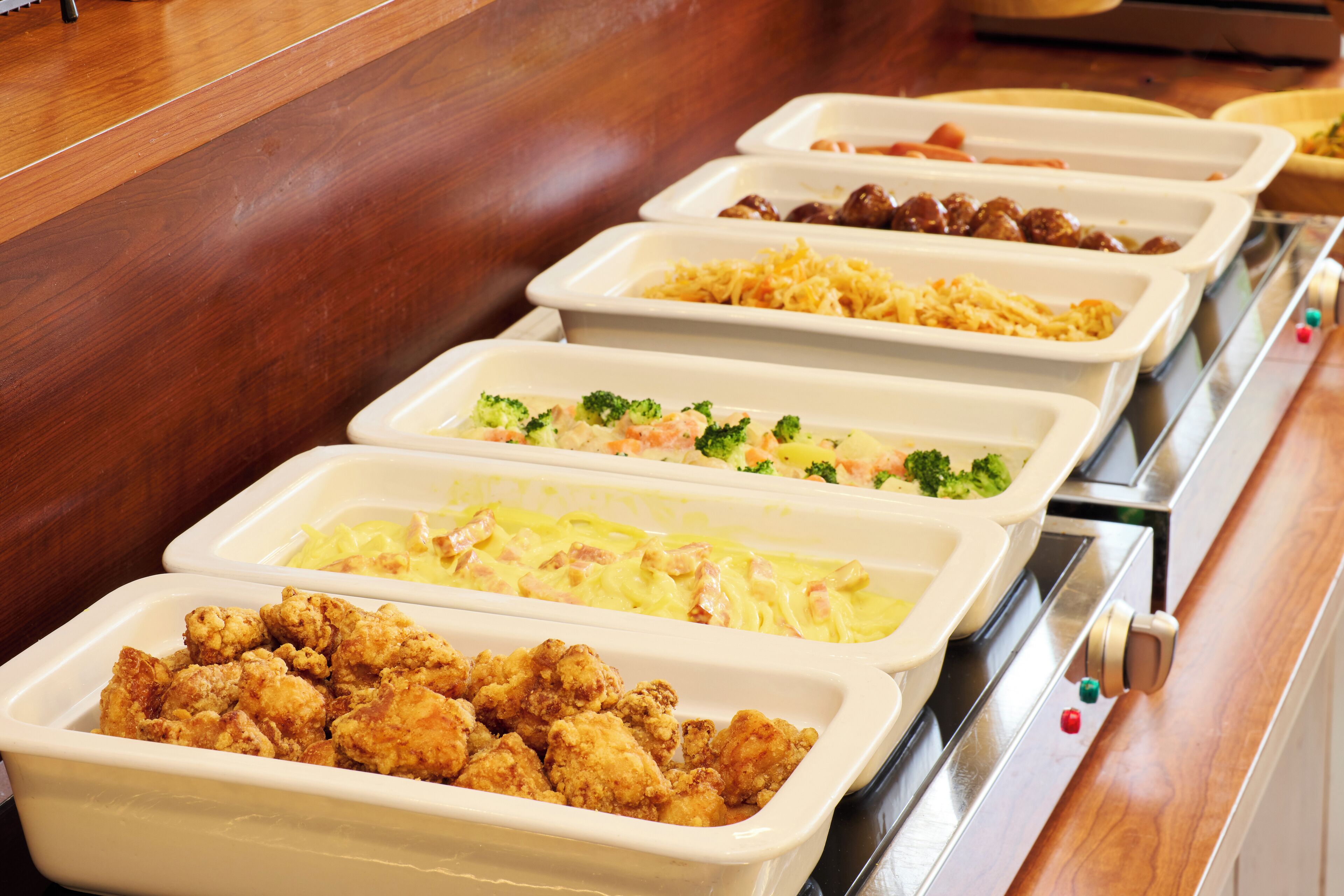 Un bufé con diversos platos, entre ellos pollo frito, pasta y ensaladas.
