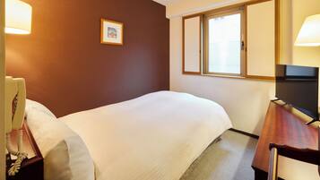 A hotel room with a bed, a desk with a lamp, a telephone, and a window with blinds.