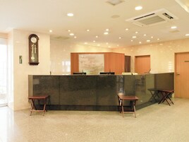 Una zona de recepción con mostrador de mármol, sillas de madera, un reloj y una puerta privada.