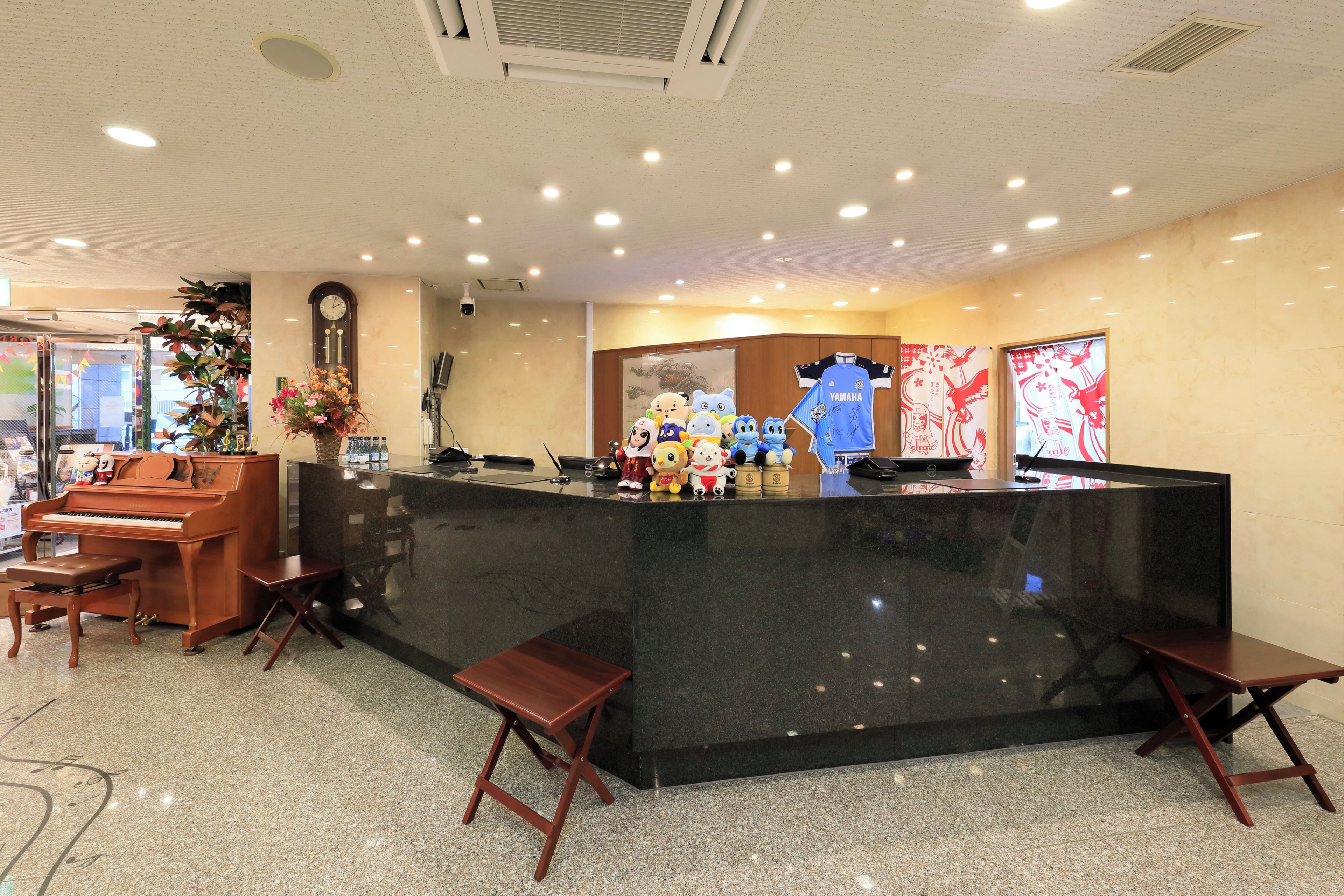 A reception area with a black marble counter, wooden chairs, a piano, and a clock on the wall.