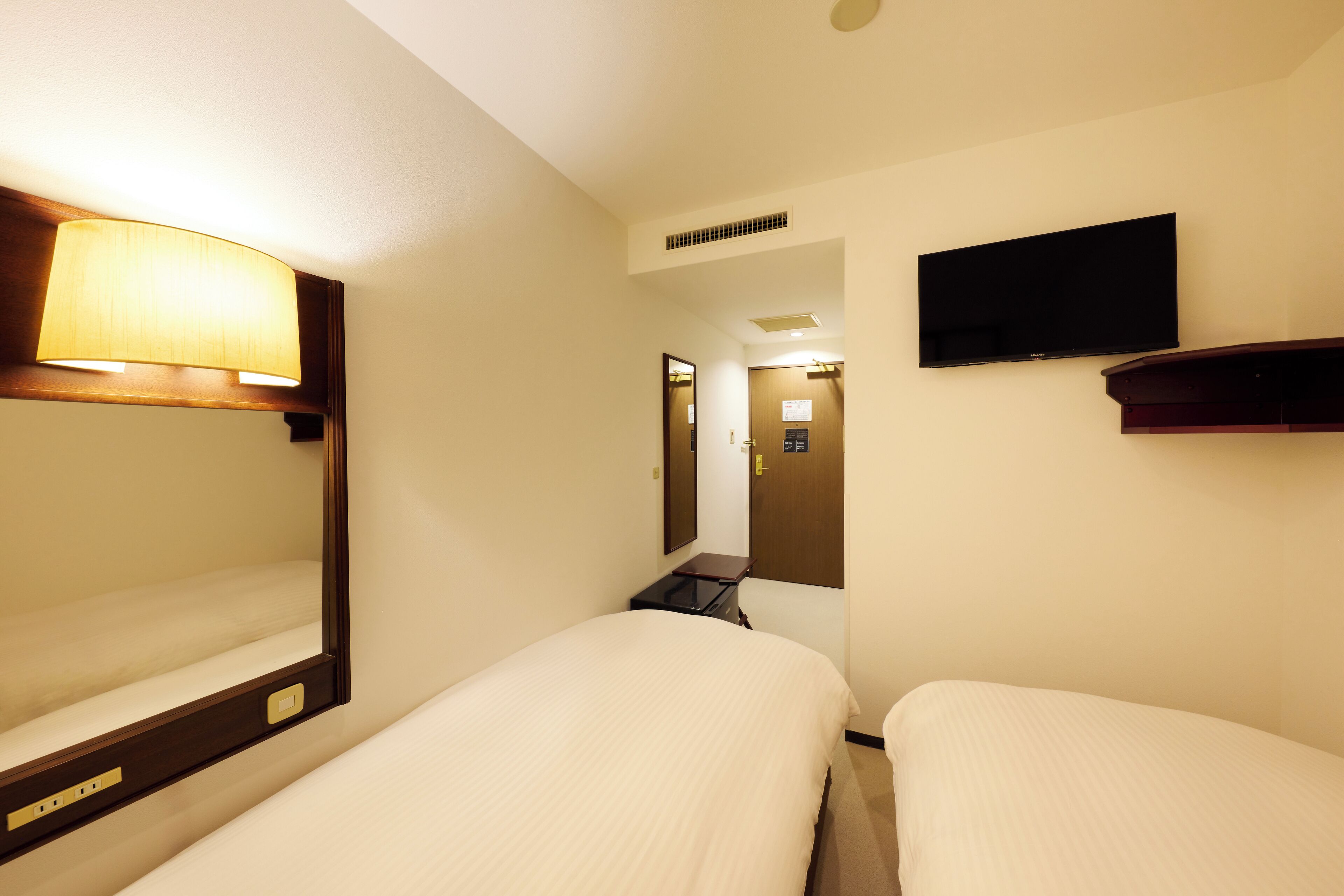 A hotel room with two beds, a television, a mirror, and a lamp.