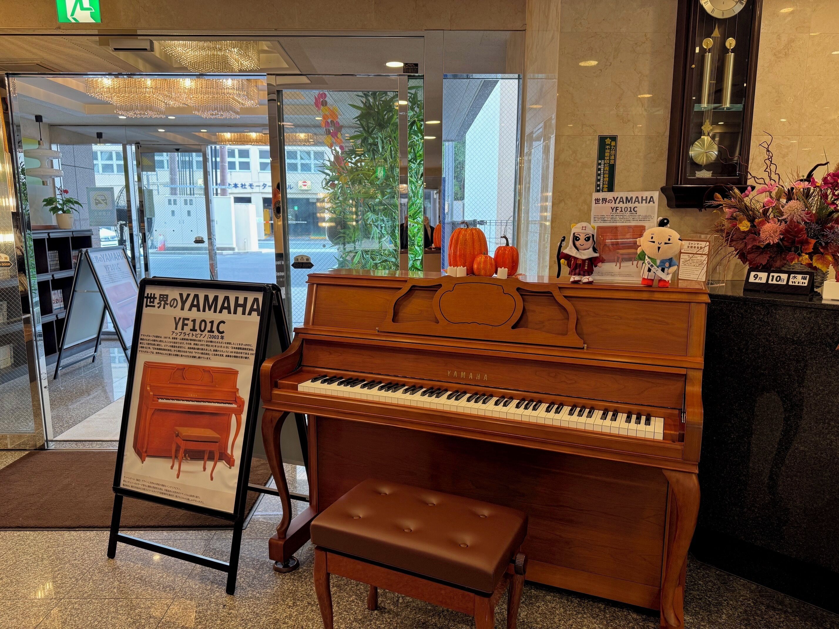 Un piano Yamaha con un banquillo en un espacio interior bien iluminado, probablemente un vestíbulo o sala de espera.