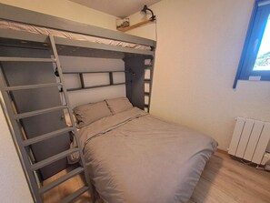A bunk bed with a ladder, a single bed below, and a window with a view.