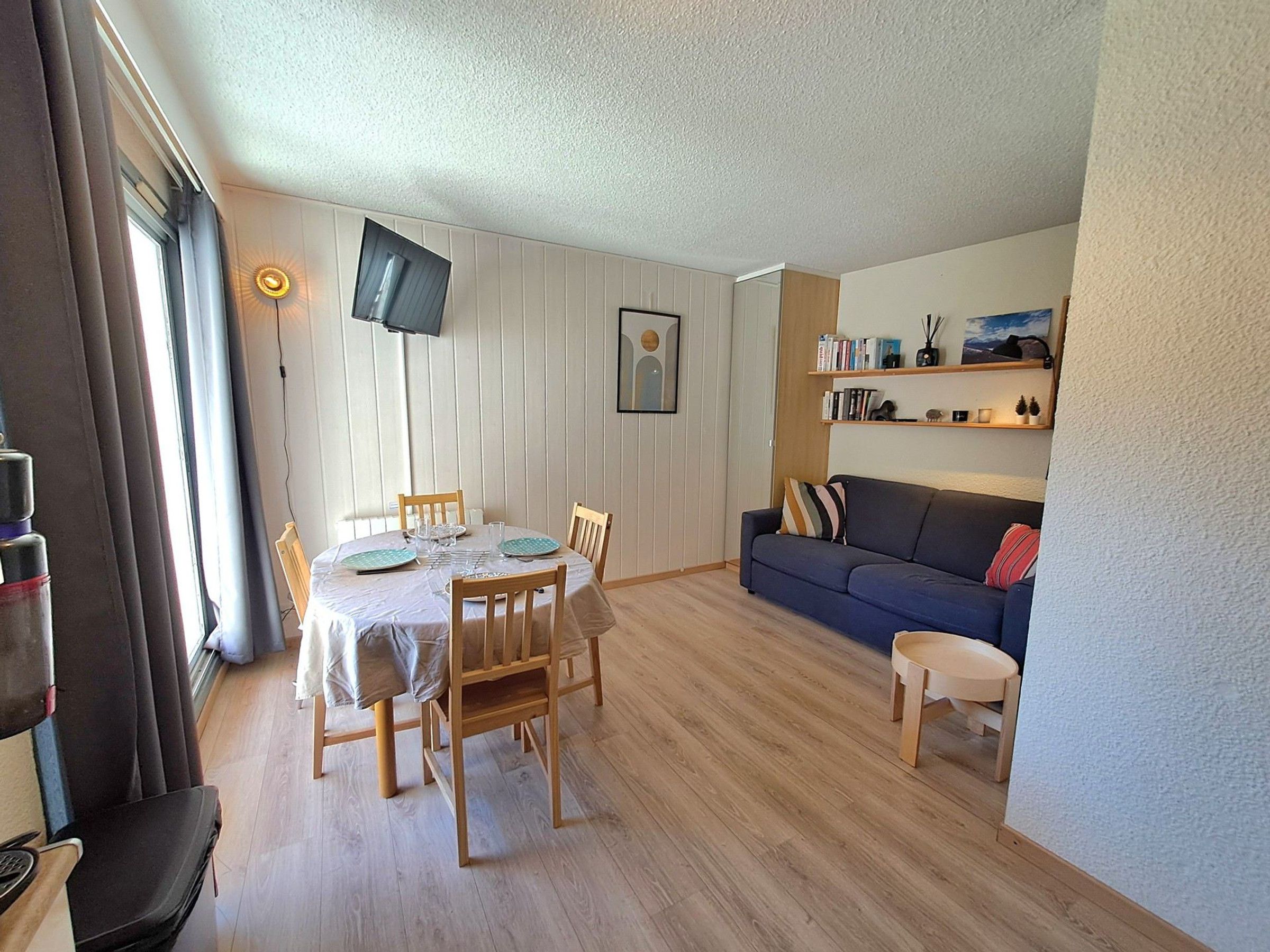 Ein Wohnzimmer mit Essbereich, einer Couch, einem an der Wand montierten Fernseher und einem Bücherregal.