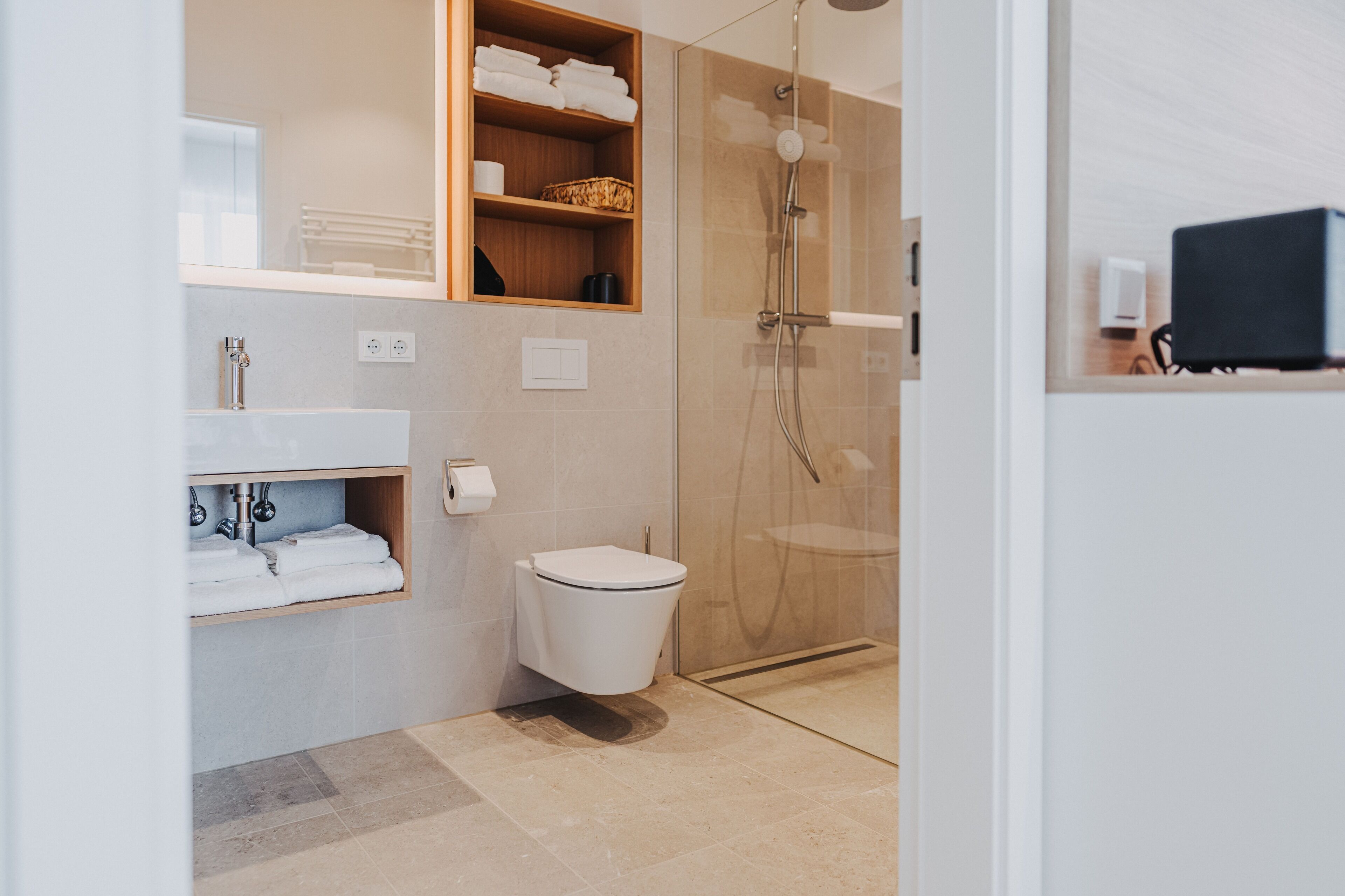 Une salle de bain moderne équipée de toilettes, d’une douche et d’étagères où sont rangées les serviettes.