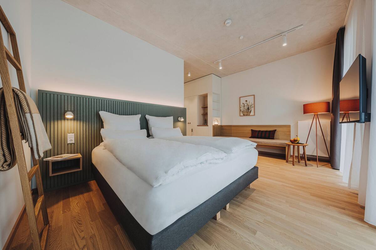A modern hotel room with a large bed, bedside tables, a desk, and a chair.