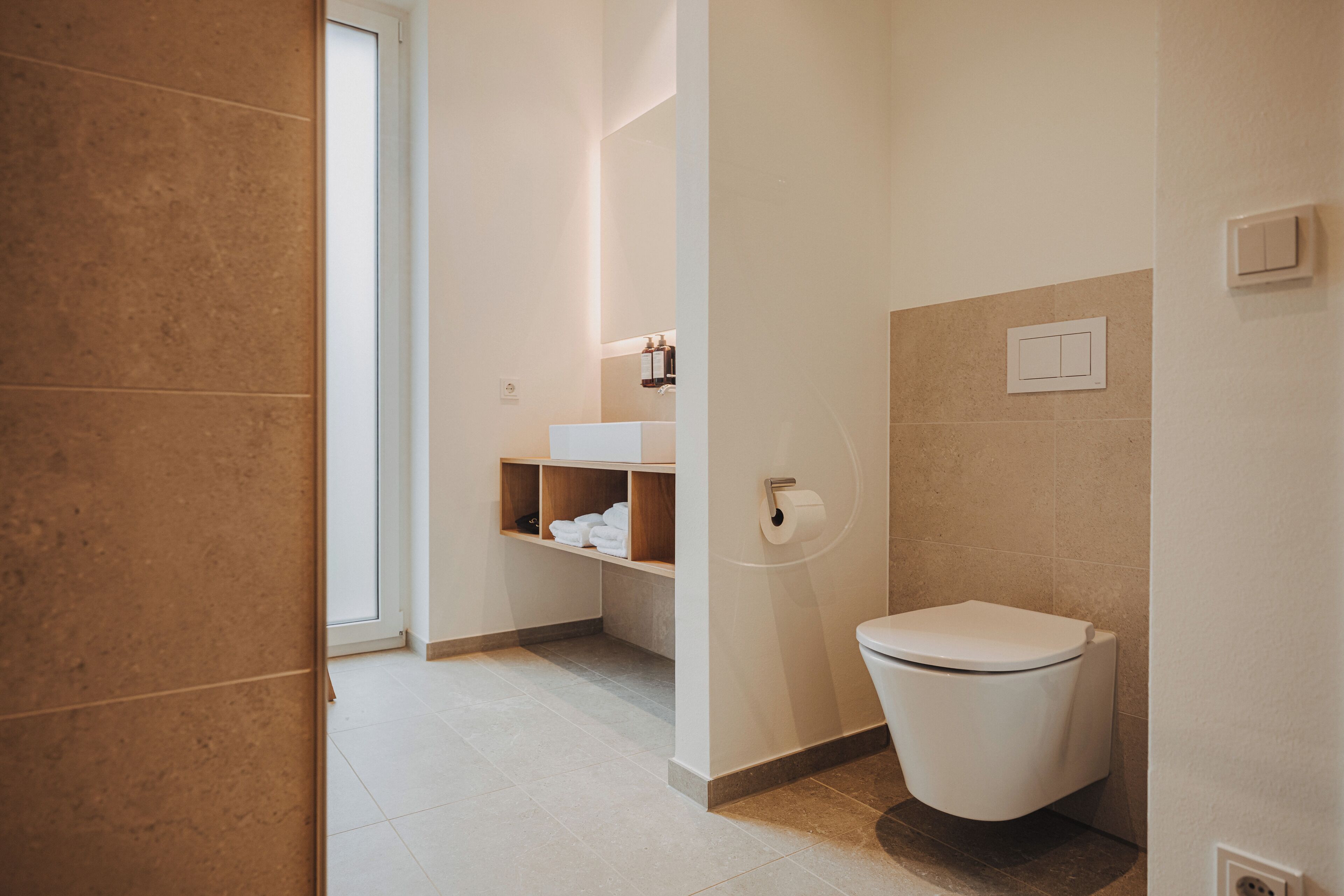 A modern bathroom with a toilet, a shelf with towels, and a toilet paper holder.